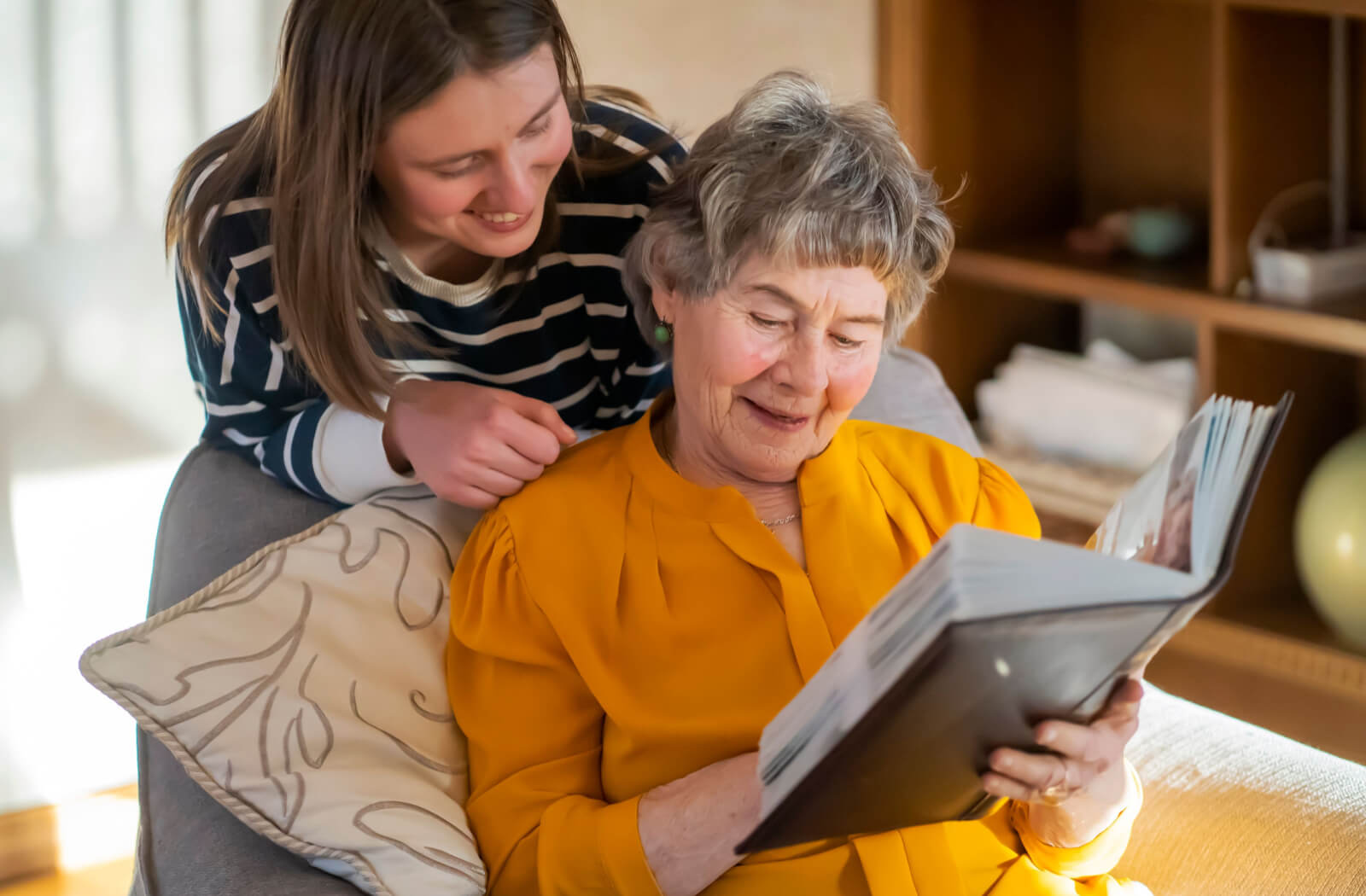 A senior woman and her daughter, smiling and looking through photo album together