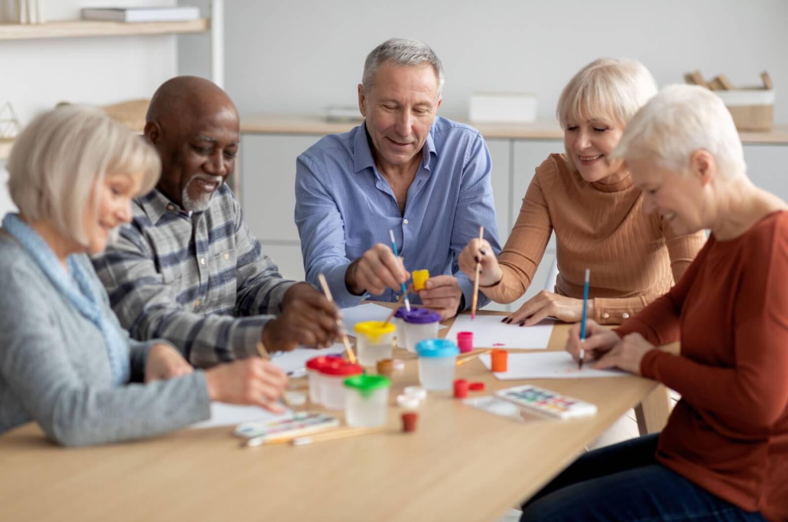 A smiling group of older adults sitting at a table and painting.