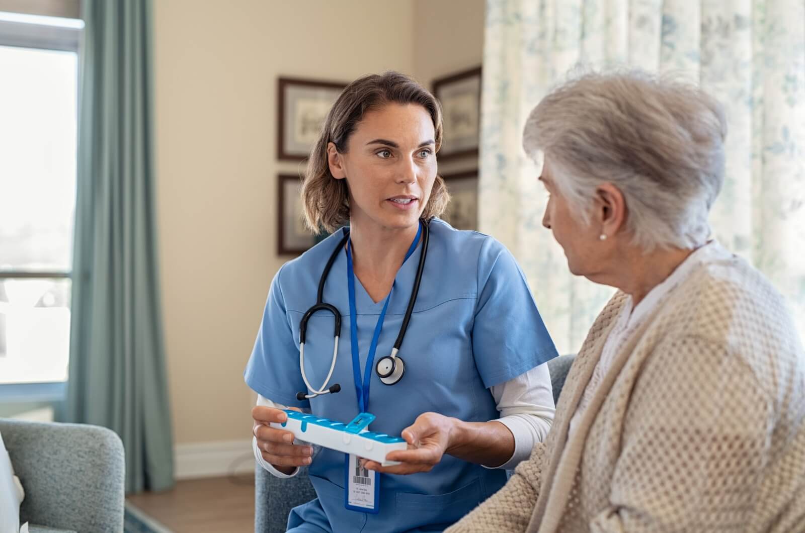 staff member in assisted living holding a pill organizer and discussing medication management with an older adult.