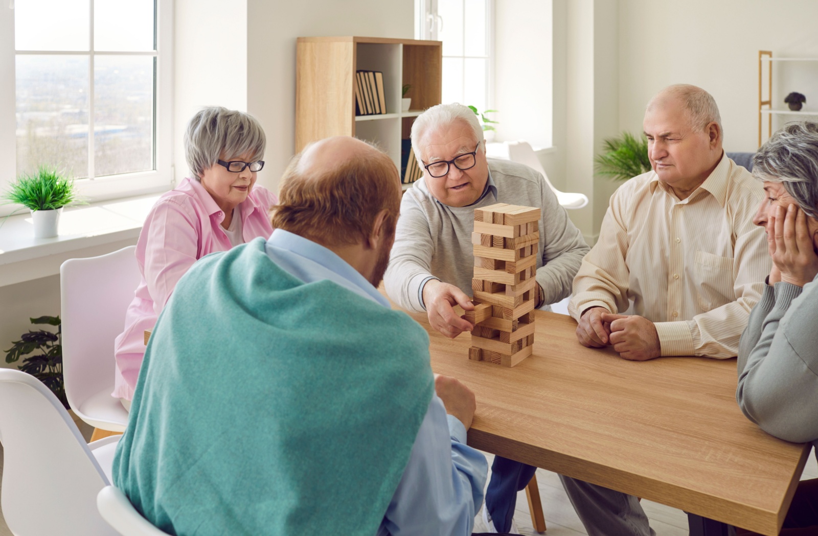 A group of 5 older adults sitting around a table and concentrating while playing jenga