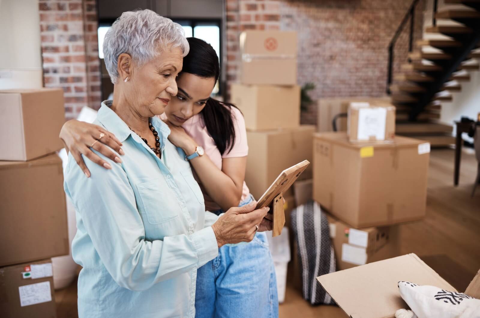 An older adult and adult child looking at a photo while packing boxes.