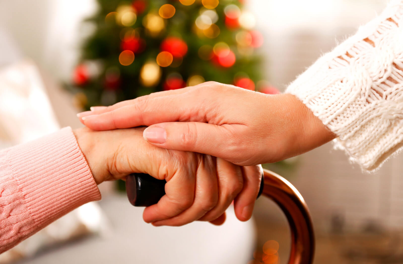 A caregiver gently touching the hand of an older adult in front of a Christmas tree in senior living.