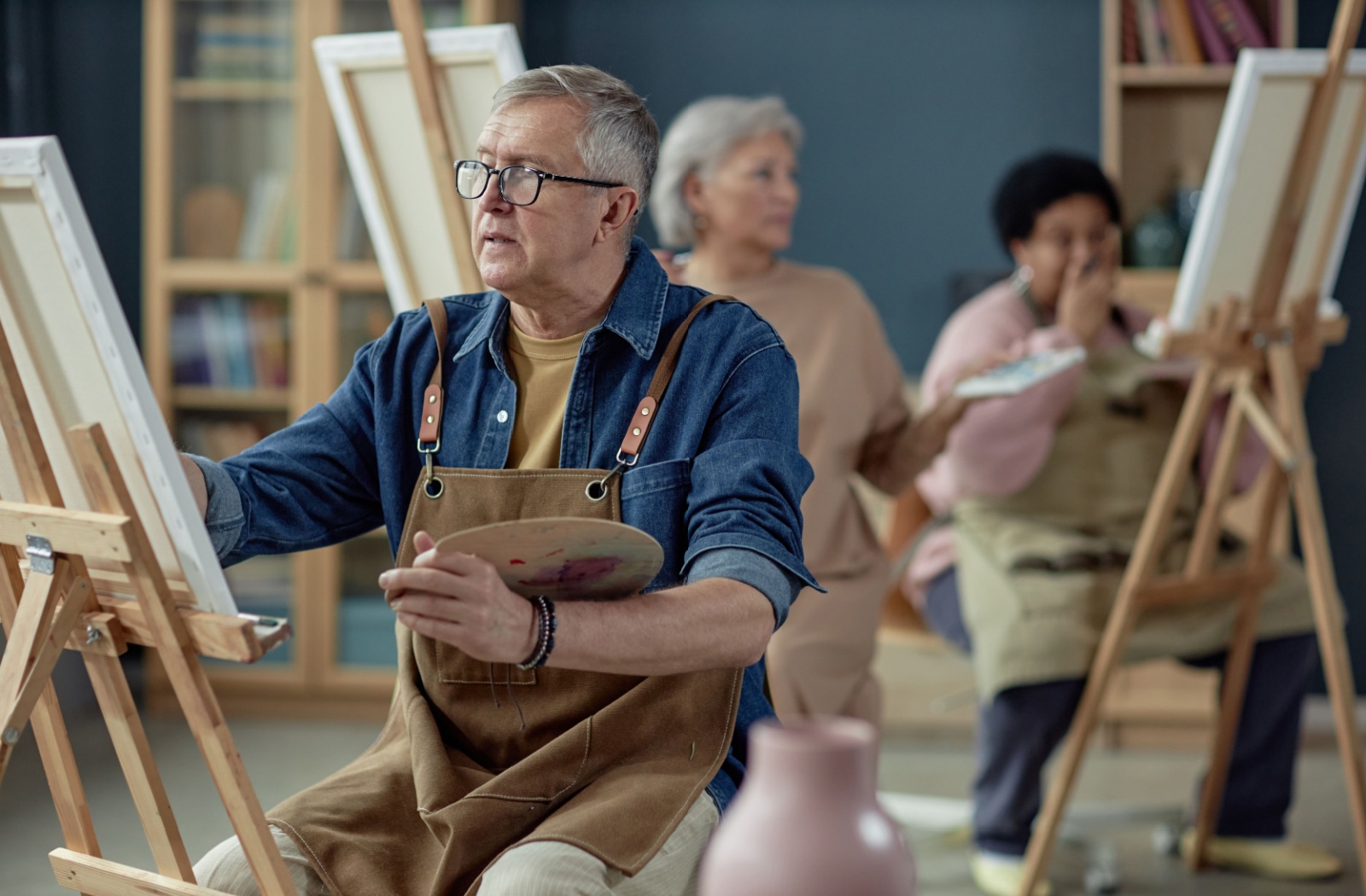 An older adult concentrates on their canvas while taking an art class within their senior living community.