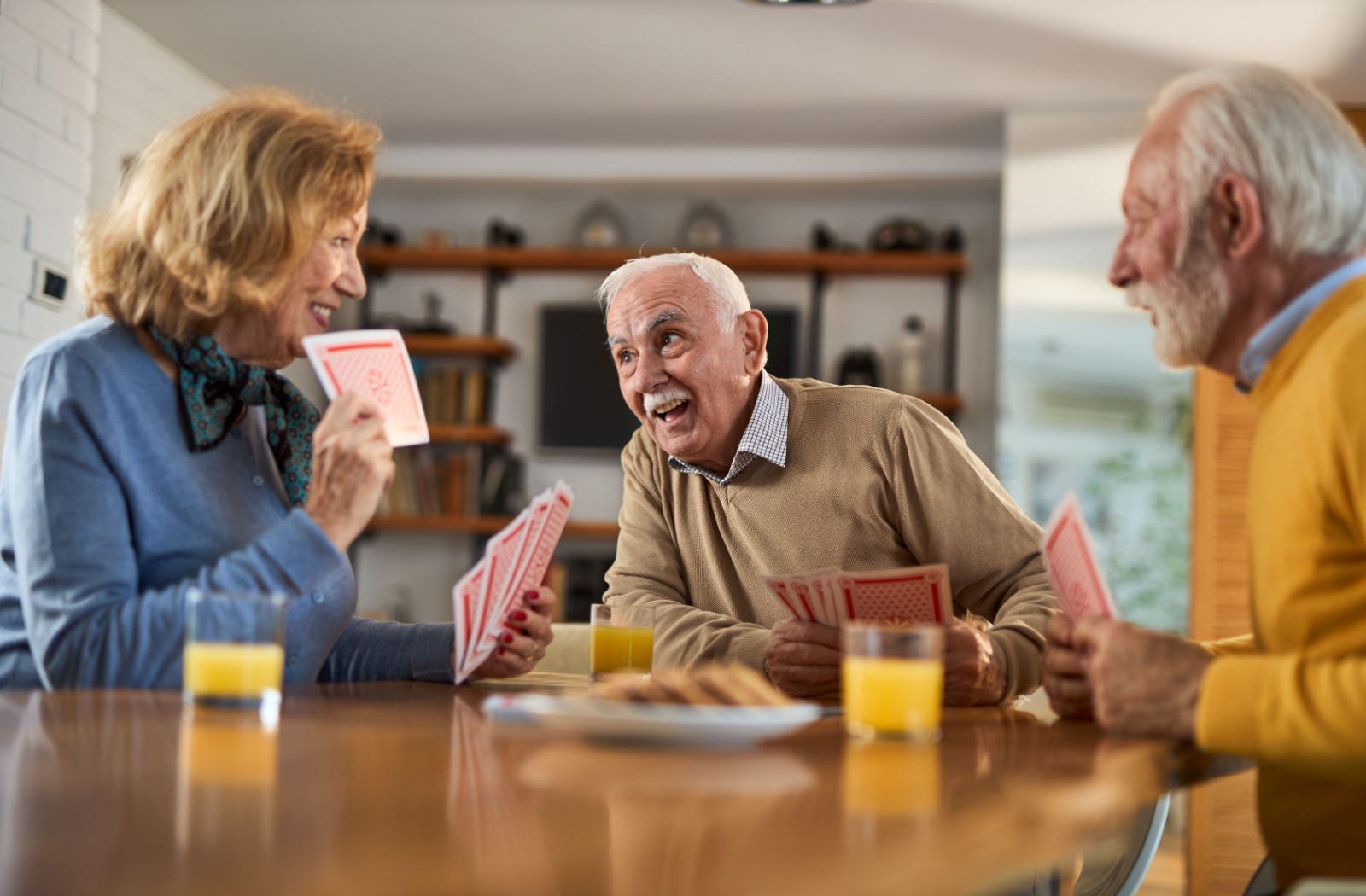 A group of seniors enjoy each other's company over a game of cards in a common area within their independent living community.