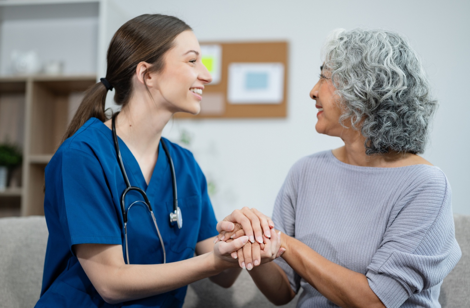 A caregiver and a senior holding hands and smiling at one another in mutual respect.