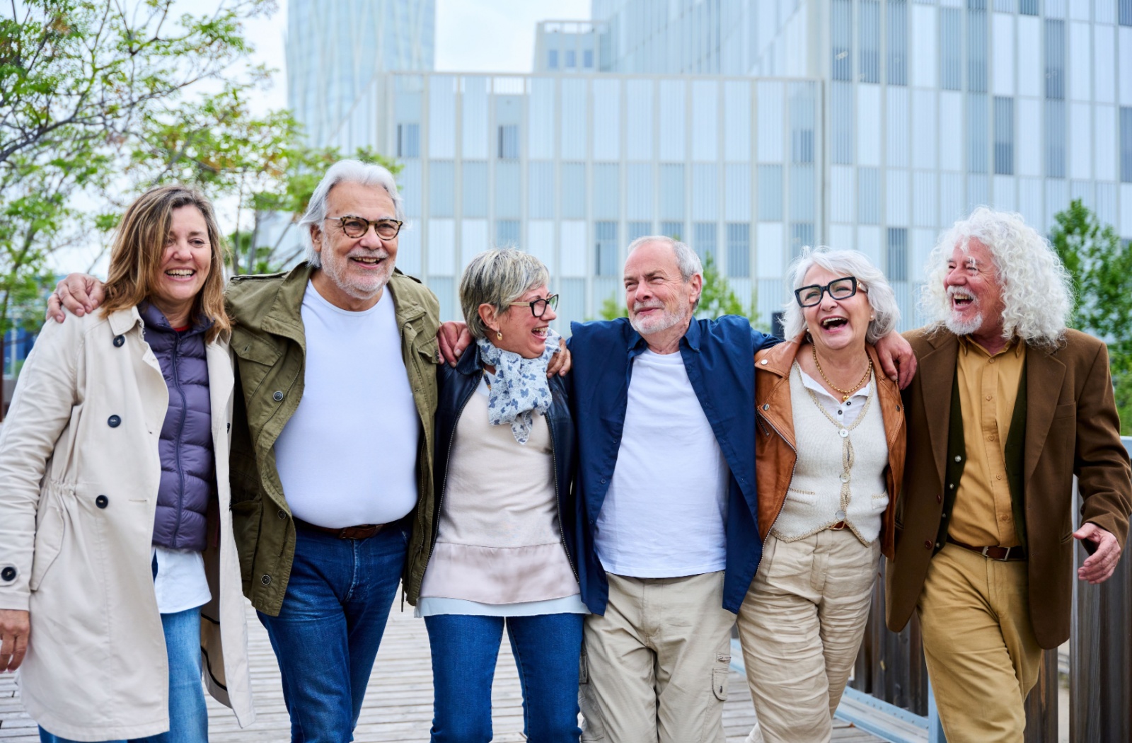 Six older adults walking arm-in-arm smiling outside a modern city building on a sunny day.