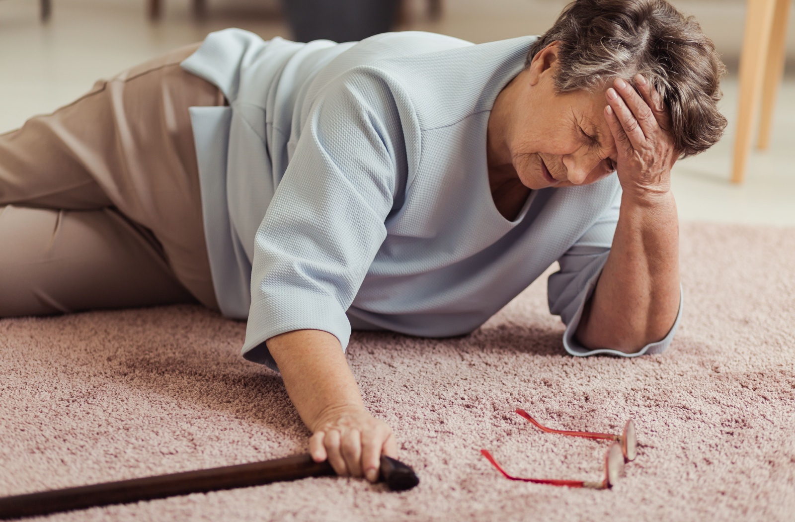 A senior expresses frustration with themselves for falling again as they reach for their cane, their glasses beside them