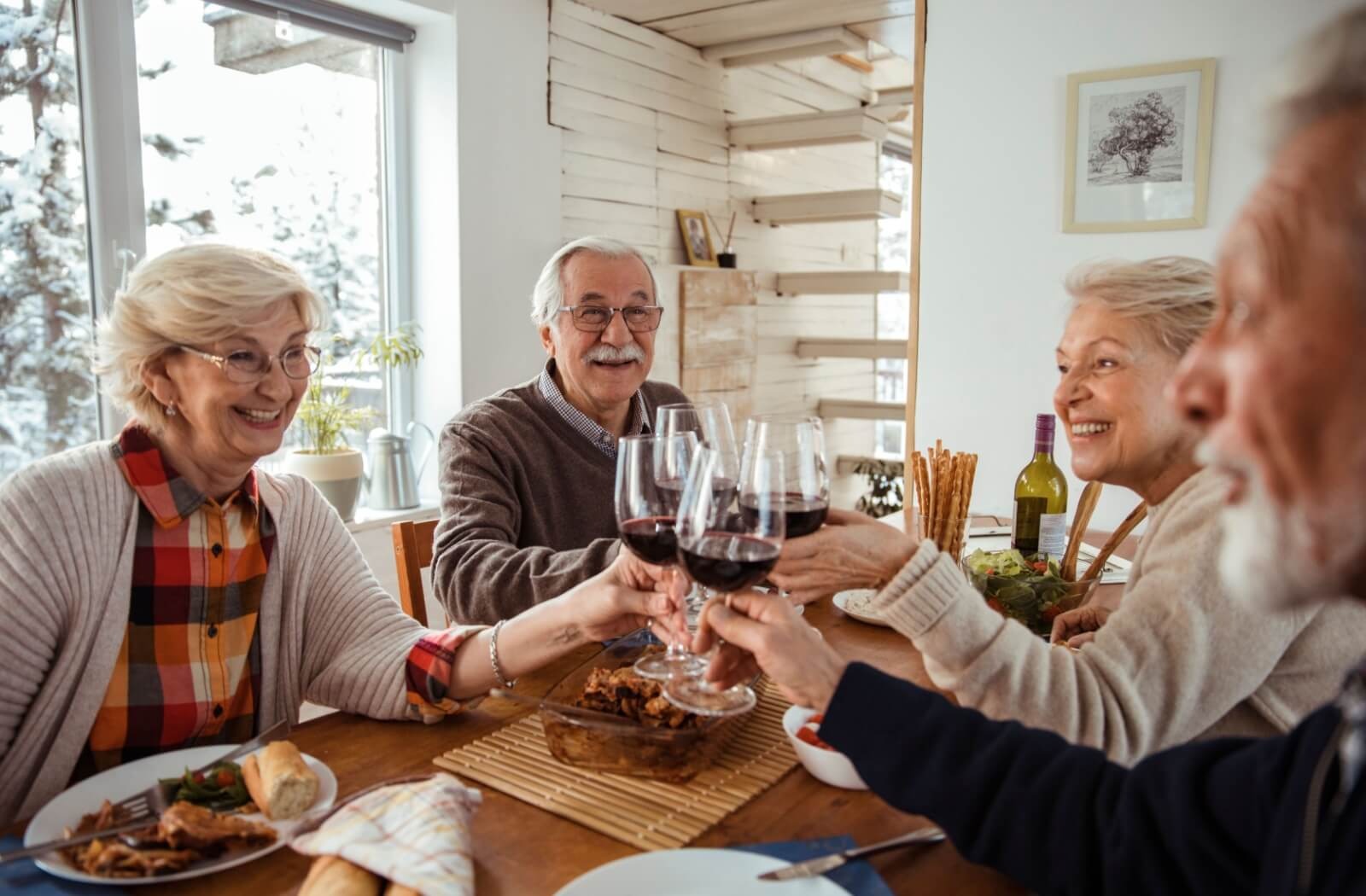 4 older adults clink glasses of wine together over a meal in a friend's home in assisted living
