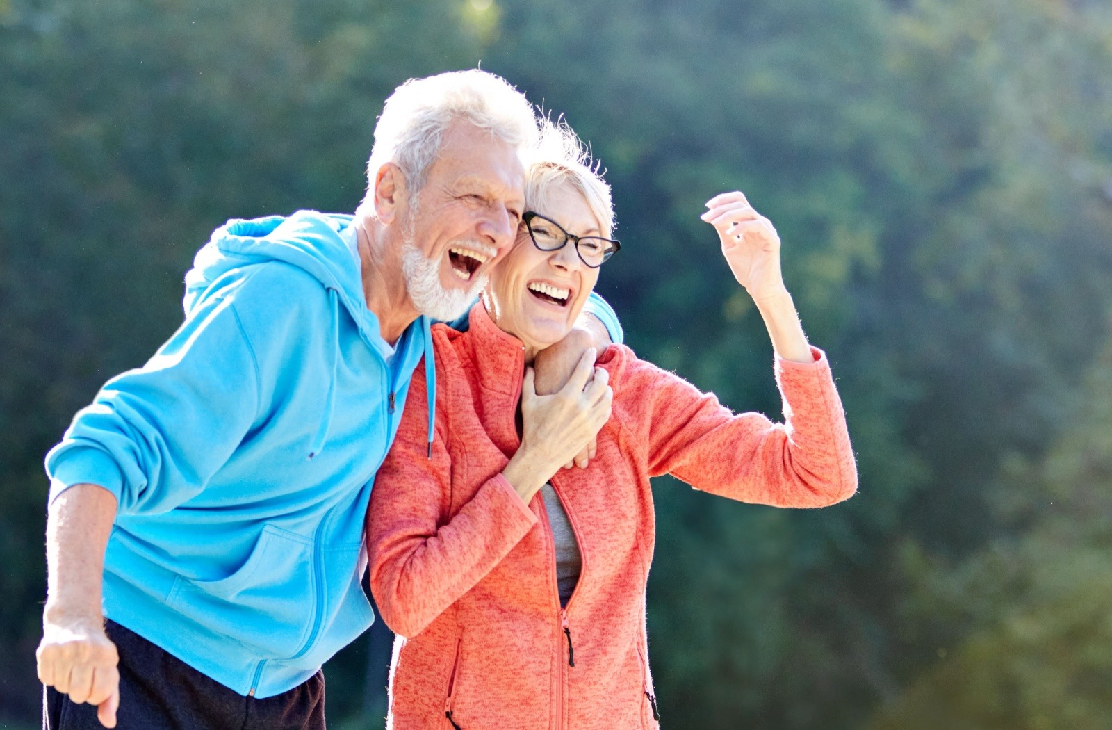 a senior couple laughs and embraces as they take a walk outside