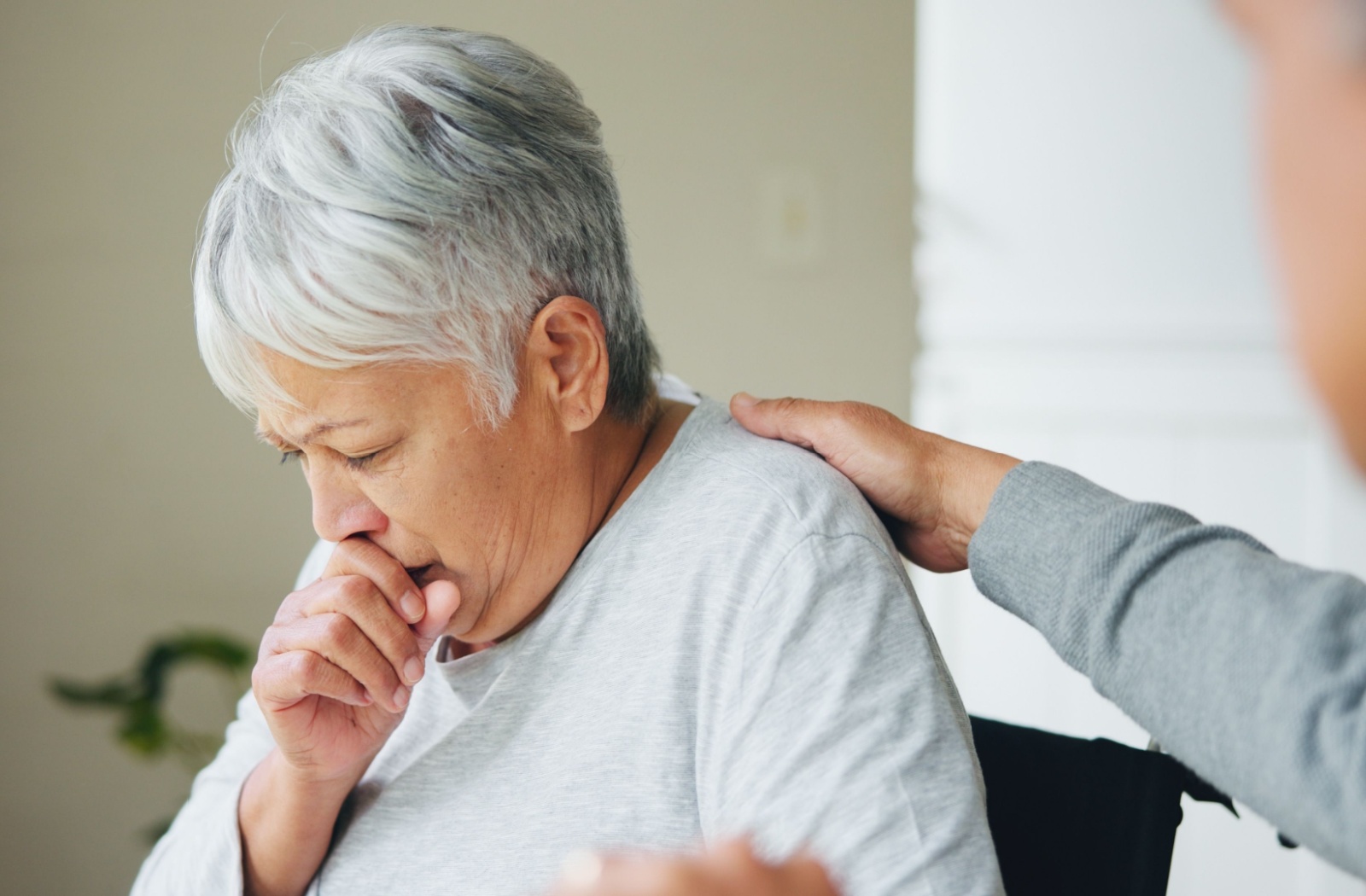A senior coughs as their spouse comforts them with a hand on their shoulder.